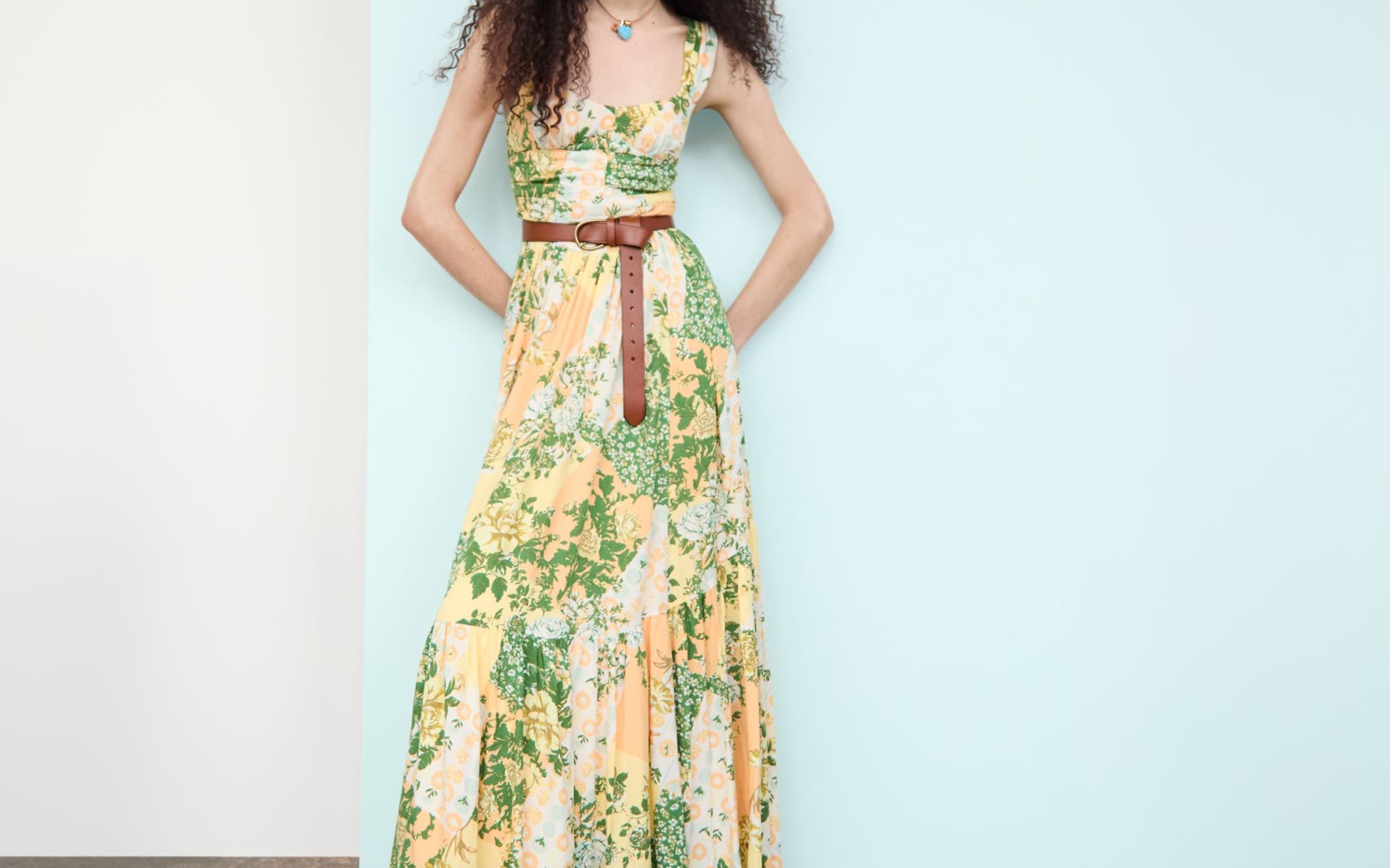 Woman wearing a printed maxi dress, pendant necklace, leather belt and woven flats.