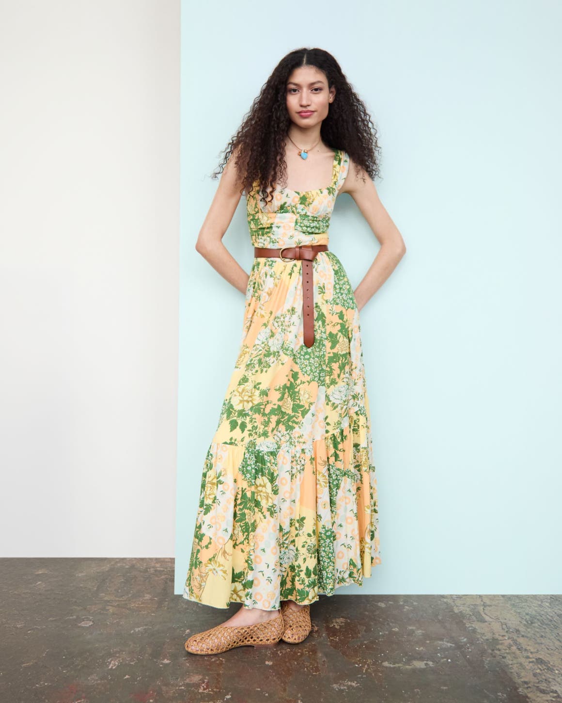 Woman wearing a printed maxi dress, pendant necklace, leather belt and woven flats.
