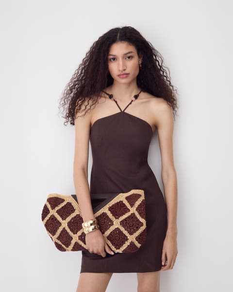 Woman wearing a brown minidress, gold bangle and woven bag.