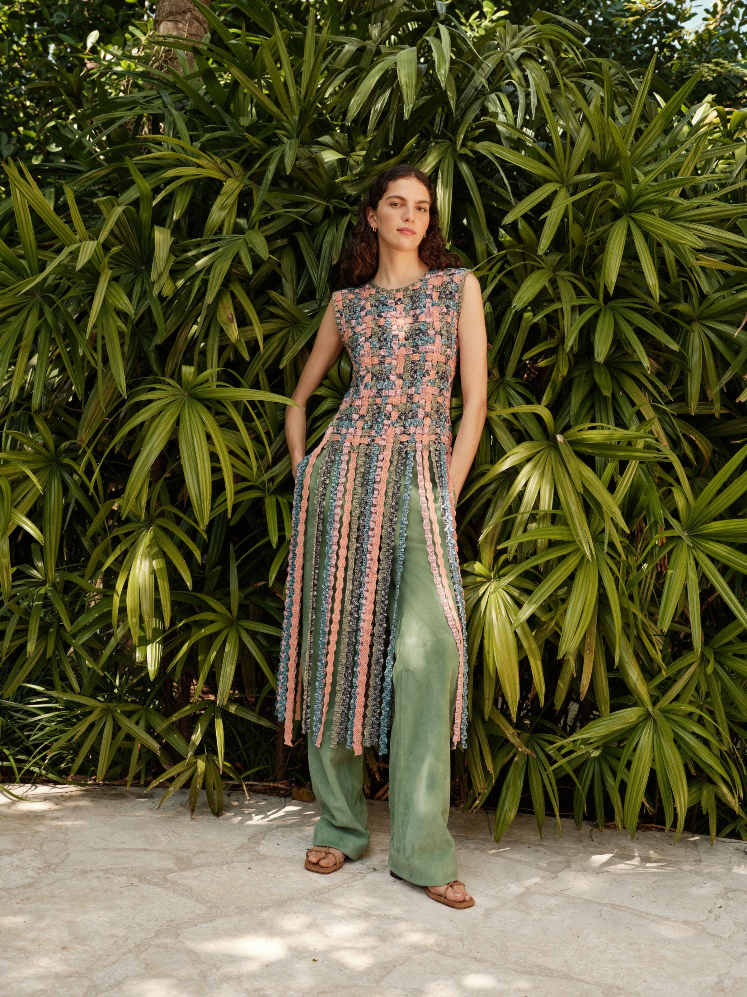 A woman wearing a woven top with fringe, suede pants and sandals.