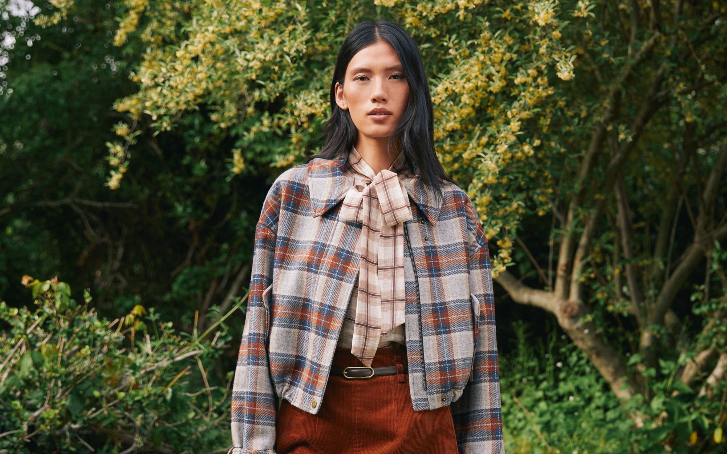 A woman wearing a plaid jacket and suede skirt.