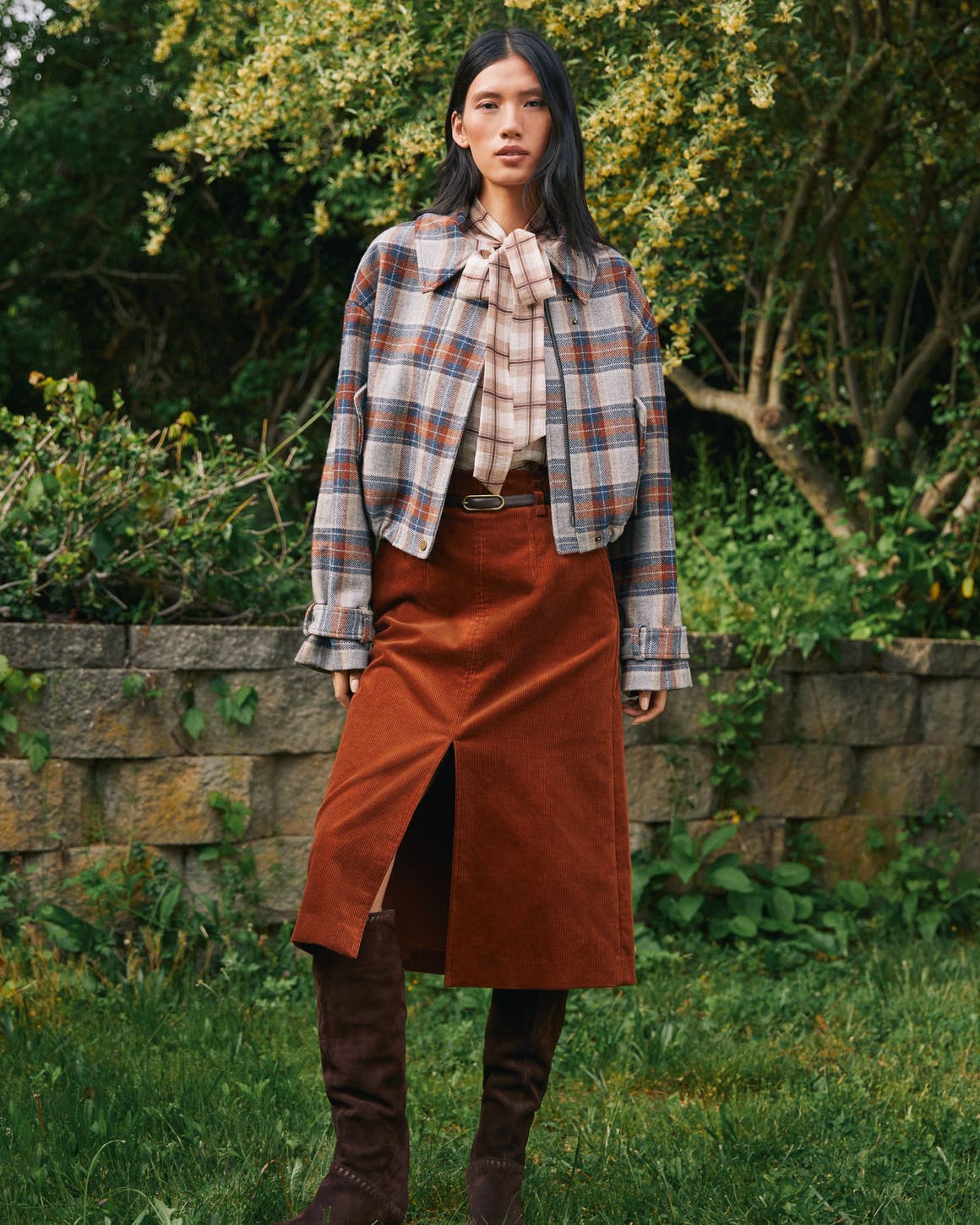 A woman wearing a plaid jacket and suede skirt.