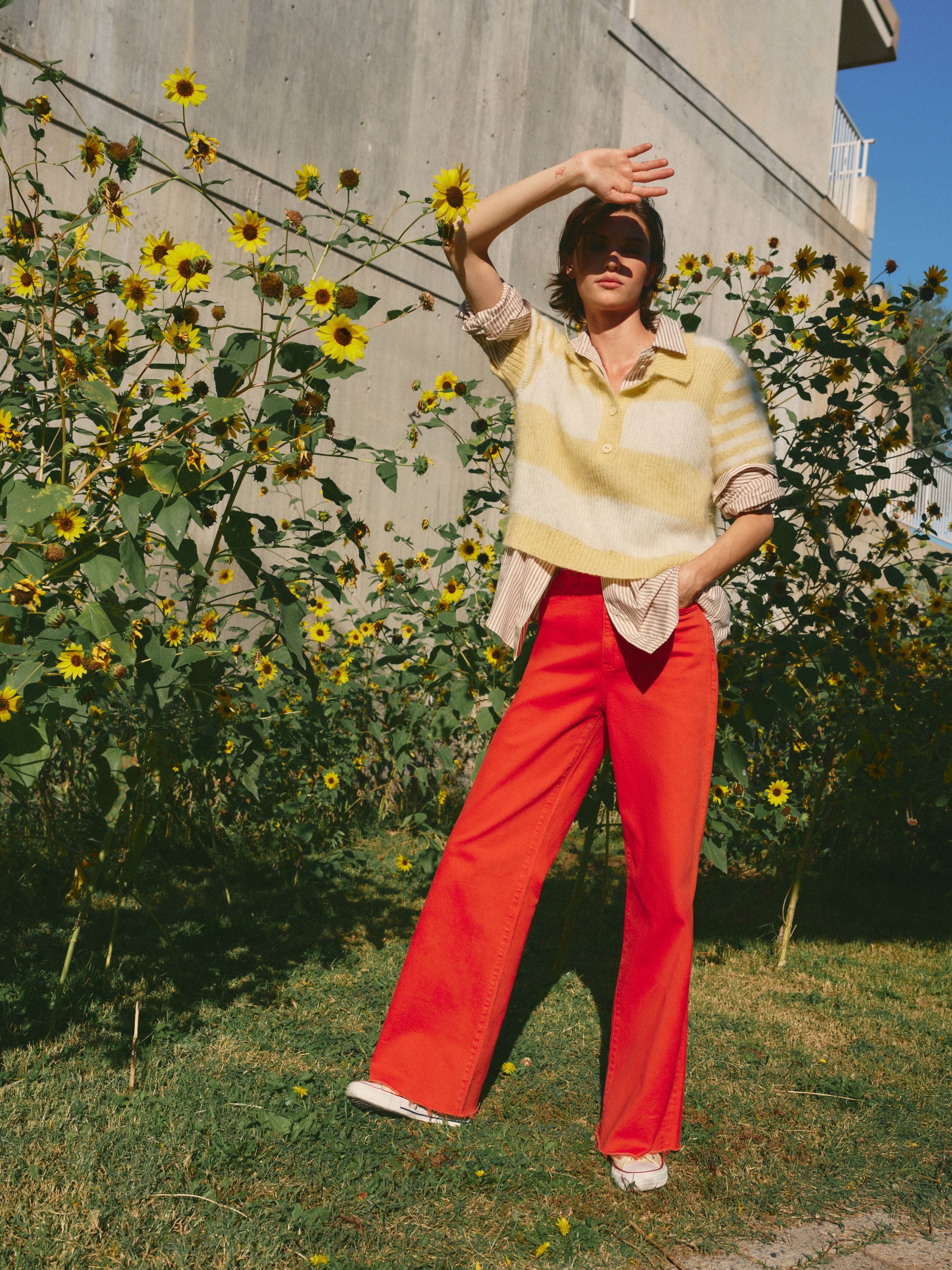 A woman wearing a yellow striped knit top over a striped button-up shirt with red pants.