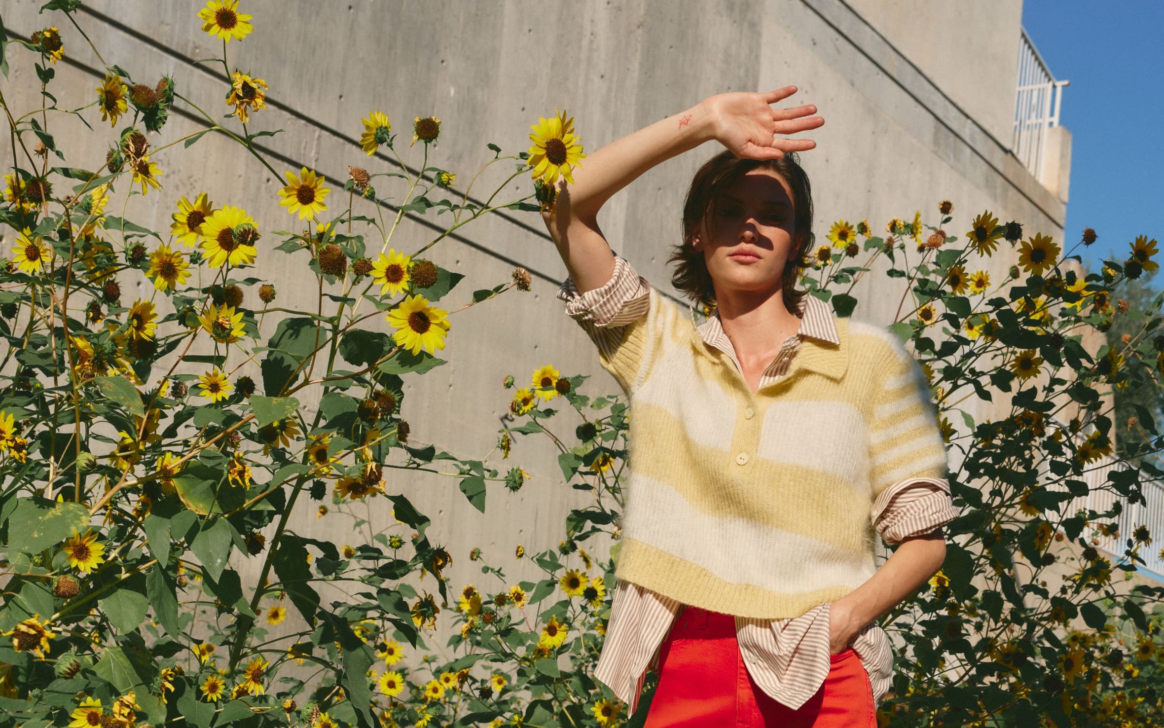 Woman wearing a pastel striped sweater over a striped shirt with red pants.