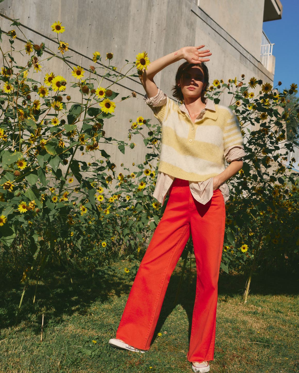Woman wearing a pastel striped sweater over a striped shirt with red pants.