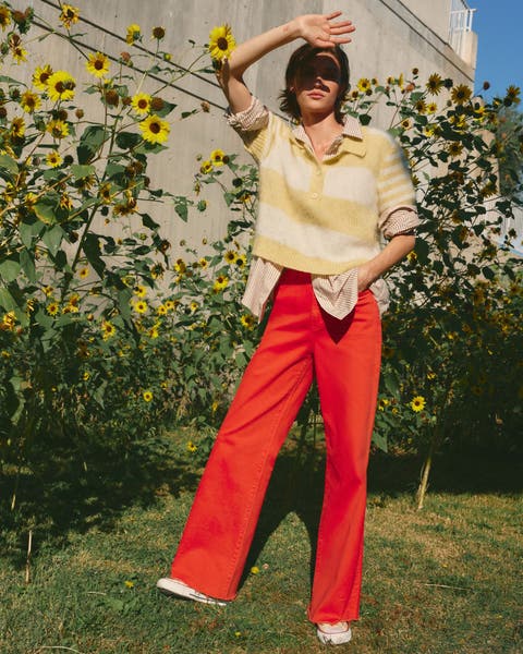 A woman wearing a yellow striped knit top over a striped button-up shirt with red pants.