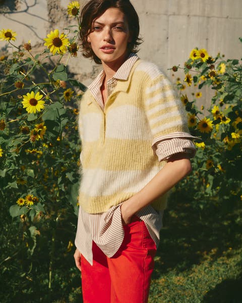 Woman wearing a striped sweater, buttoned shirt and red pants.