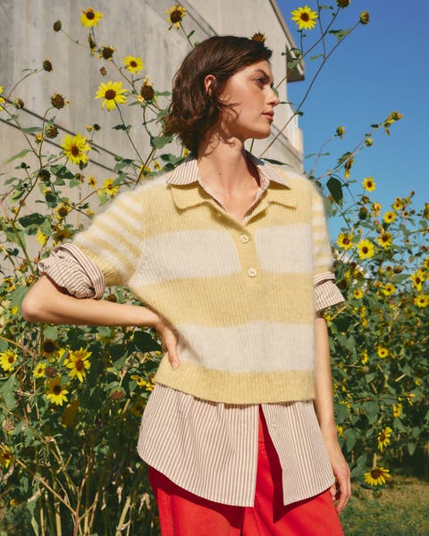 Woman wearing a pastel striped sweater over a striped shirt with red pants.