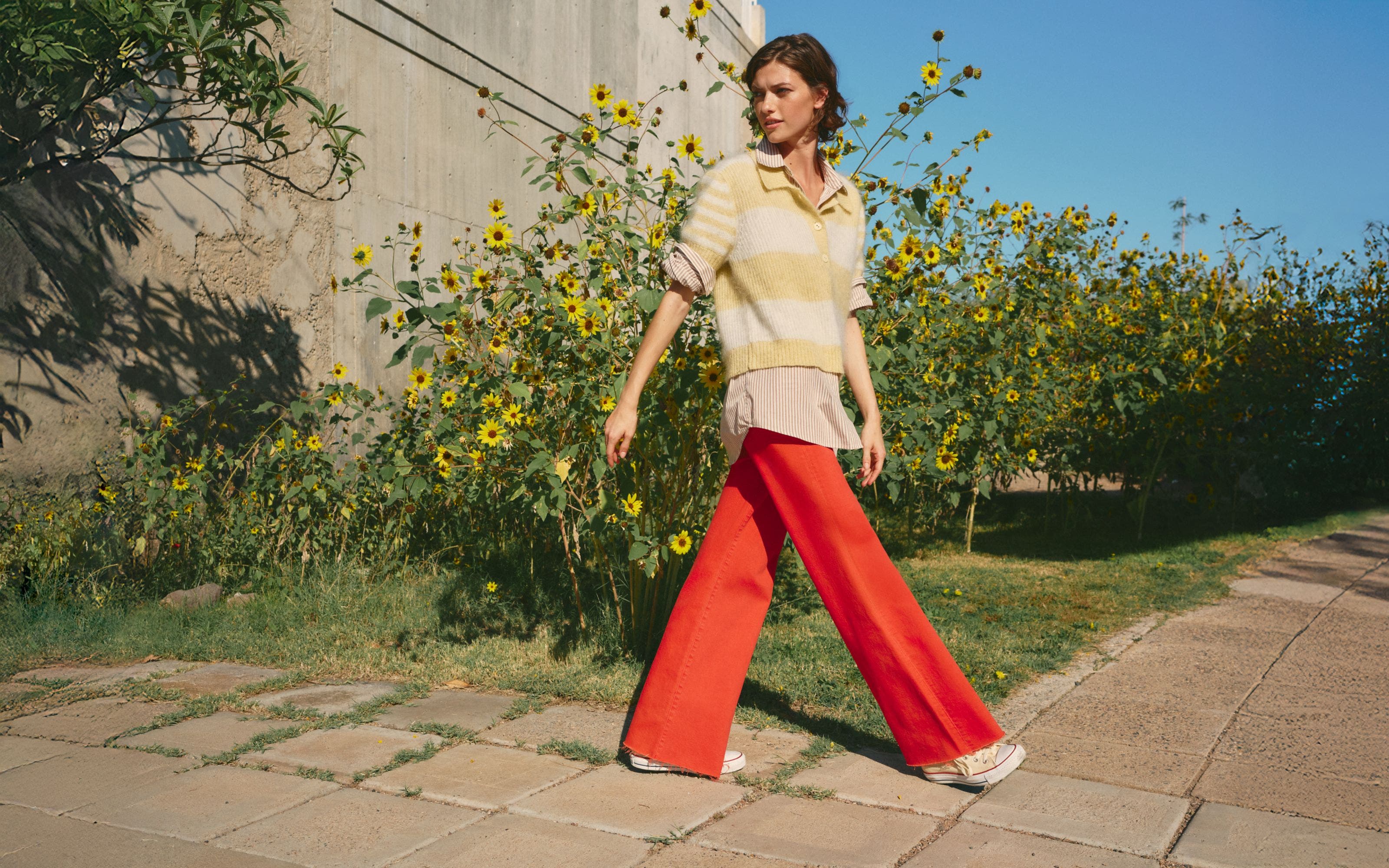Woman wearing a striped sweater, buttoned shirt and red pants.