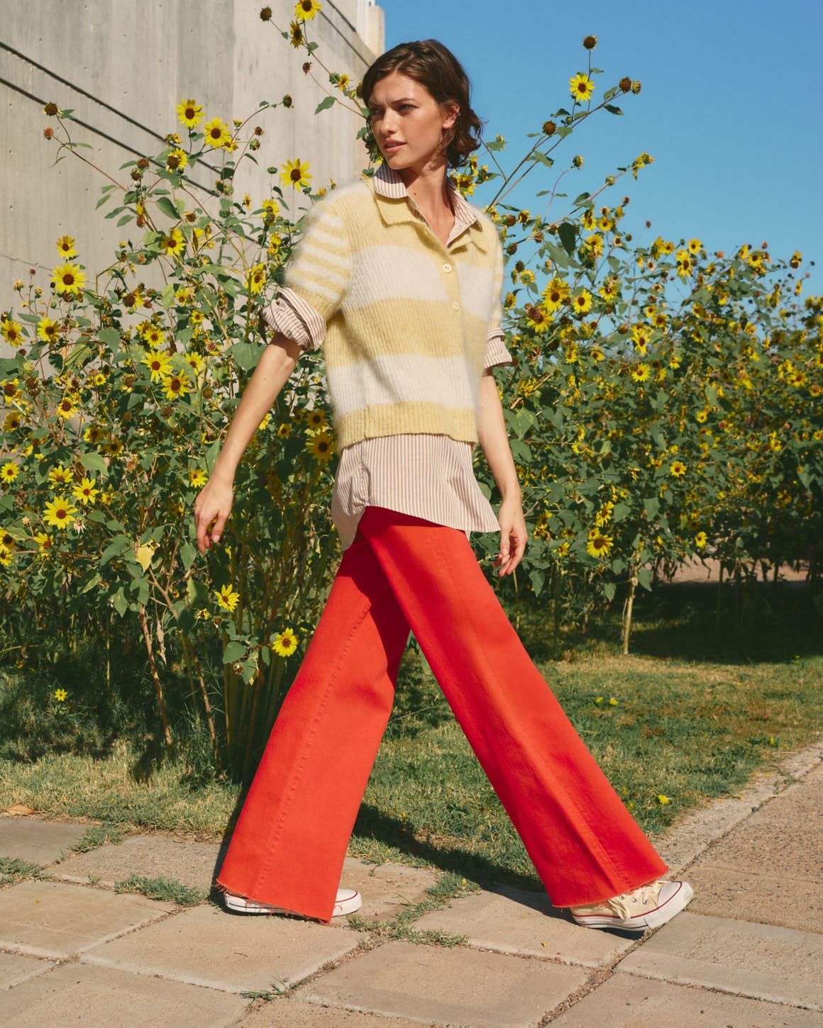 Woman wearing a striped sweater, buttoned shirt and red pants.