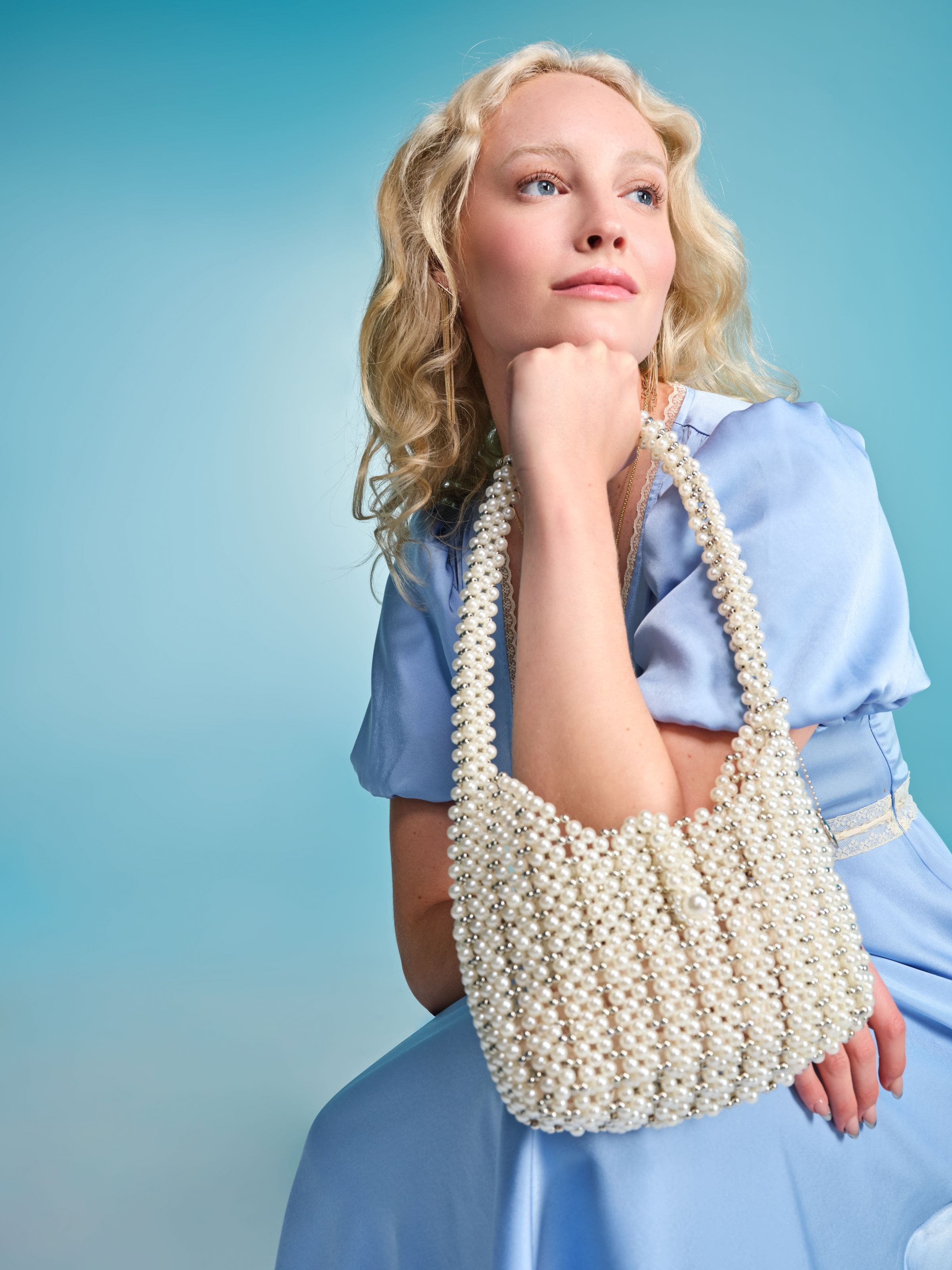 A woman holding an ivory beaded shoulder bag.