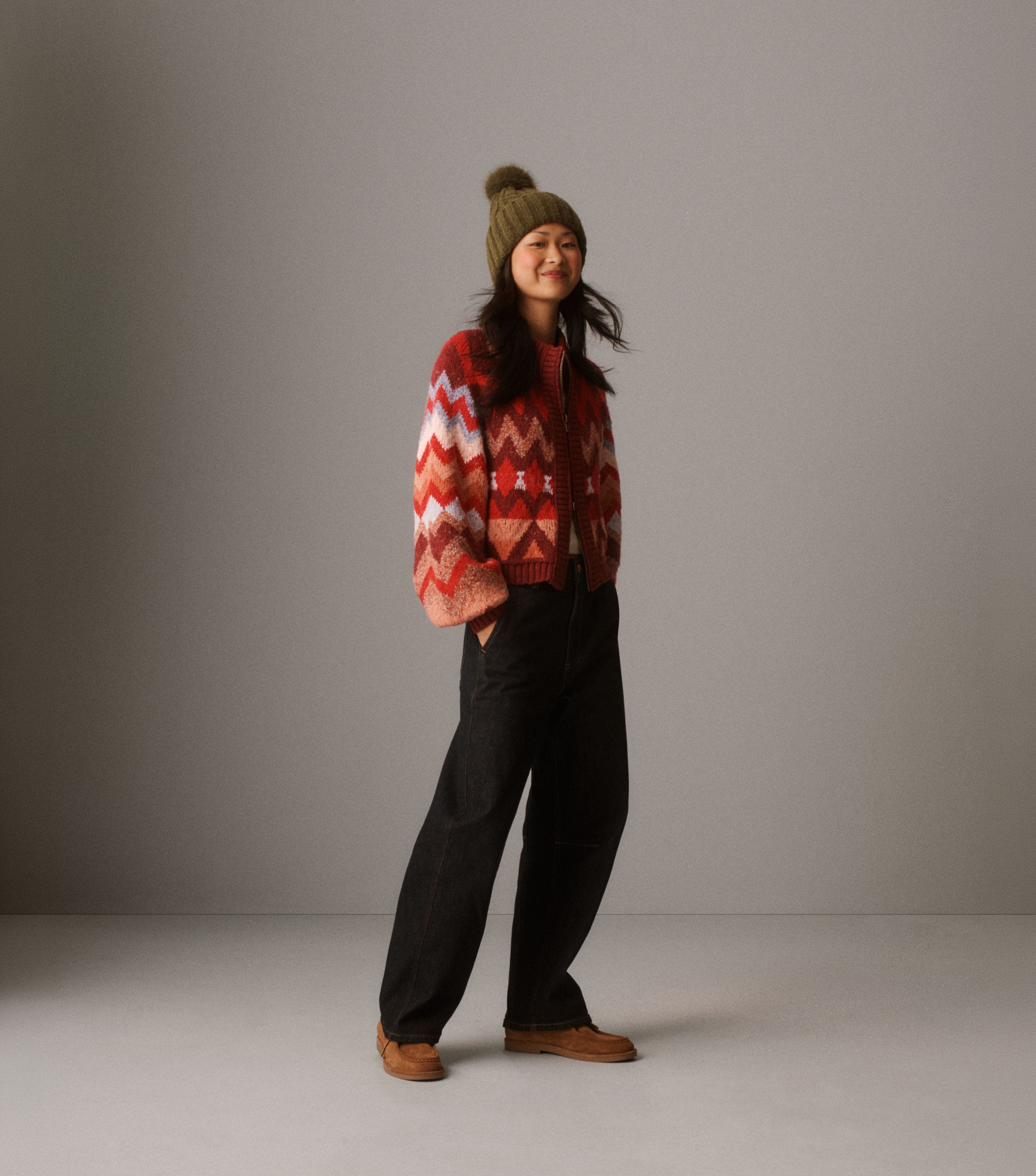 A woman wearing a festive cardigan, jeans, and beanie.