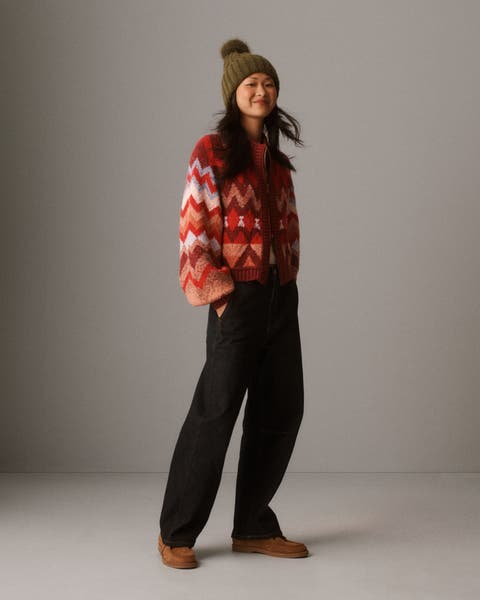 A woman wearing a red patterned cardigan, jeans, and beanie.