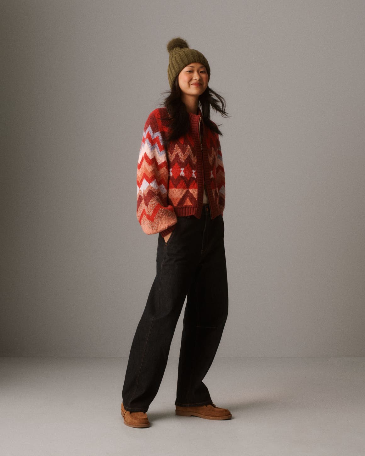 A woman wearing a festive cardigan, jeans, and beanie.