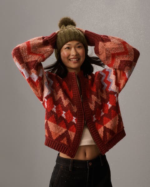 A woman wearing a patterned red cardigan and beanie.