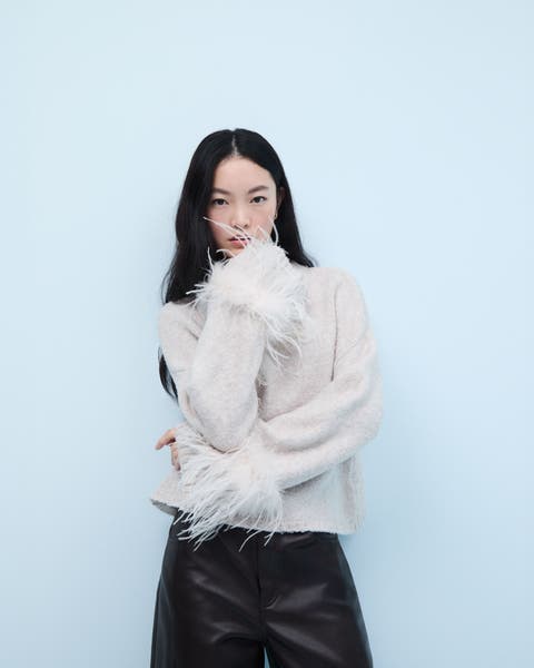 Woman wearing a sweater with feather trim and leather pants.