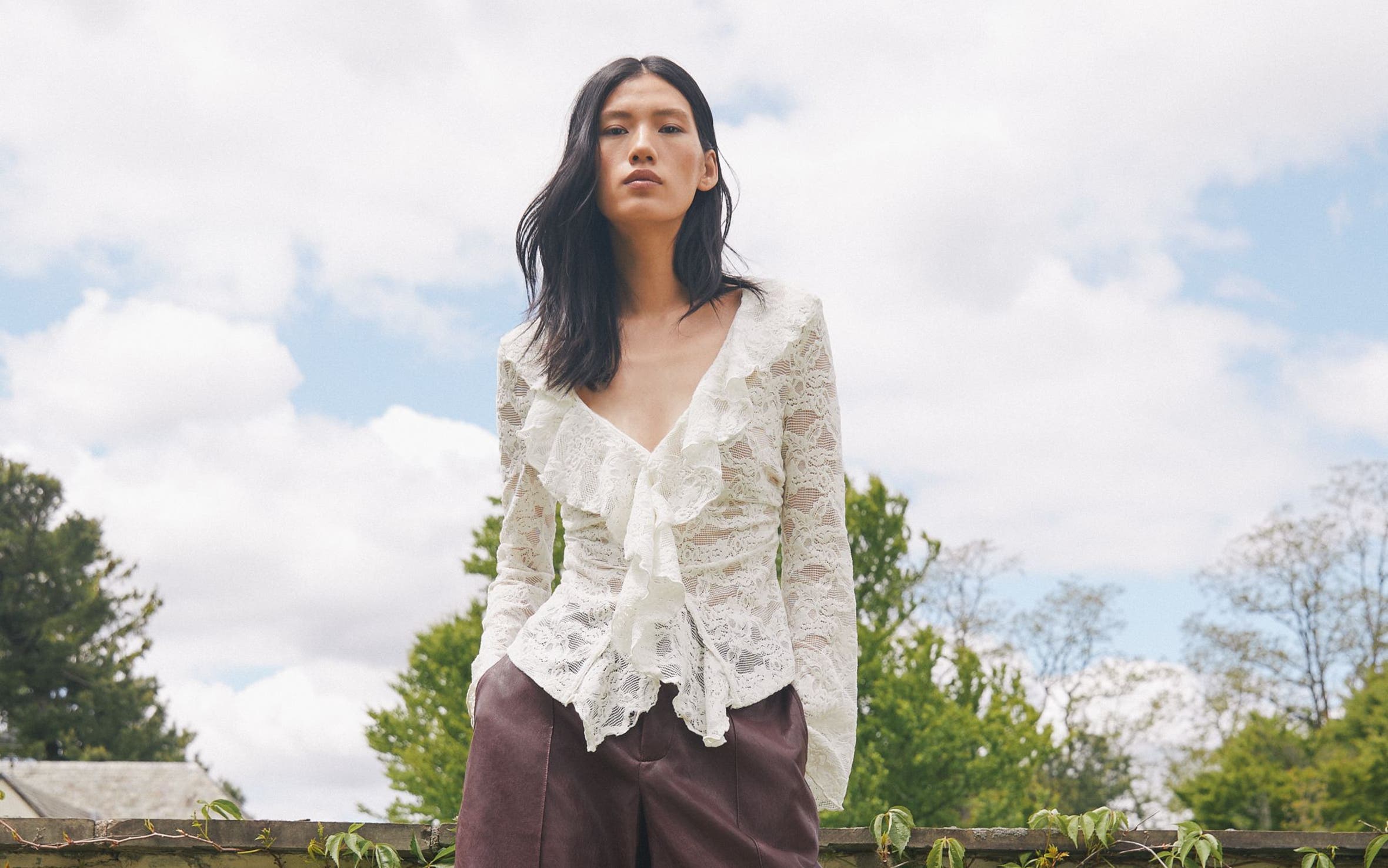 A woman wearing a lacy blouse and brown culottes.
