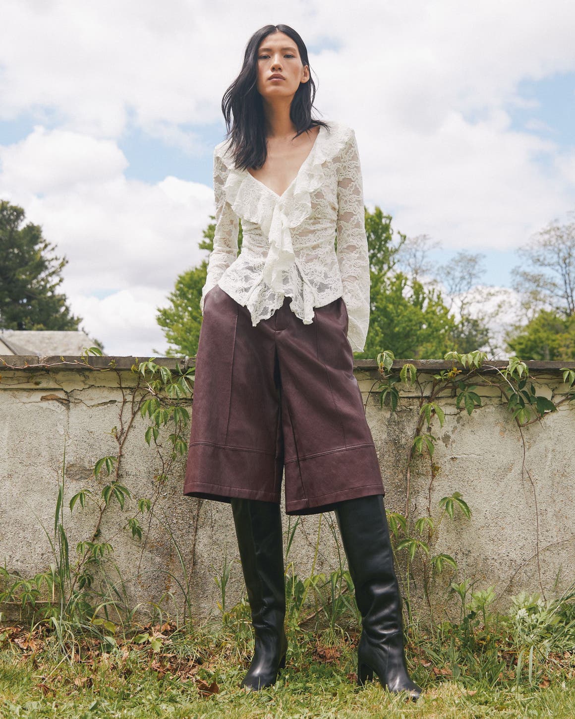 A woman wearing a lacy blouse and brown culottes.