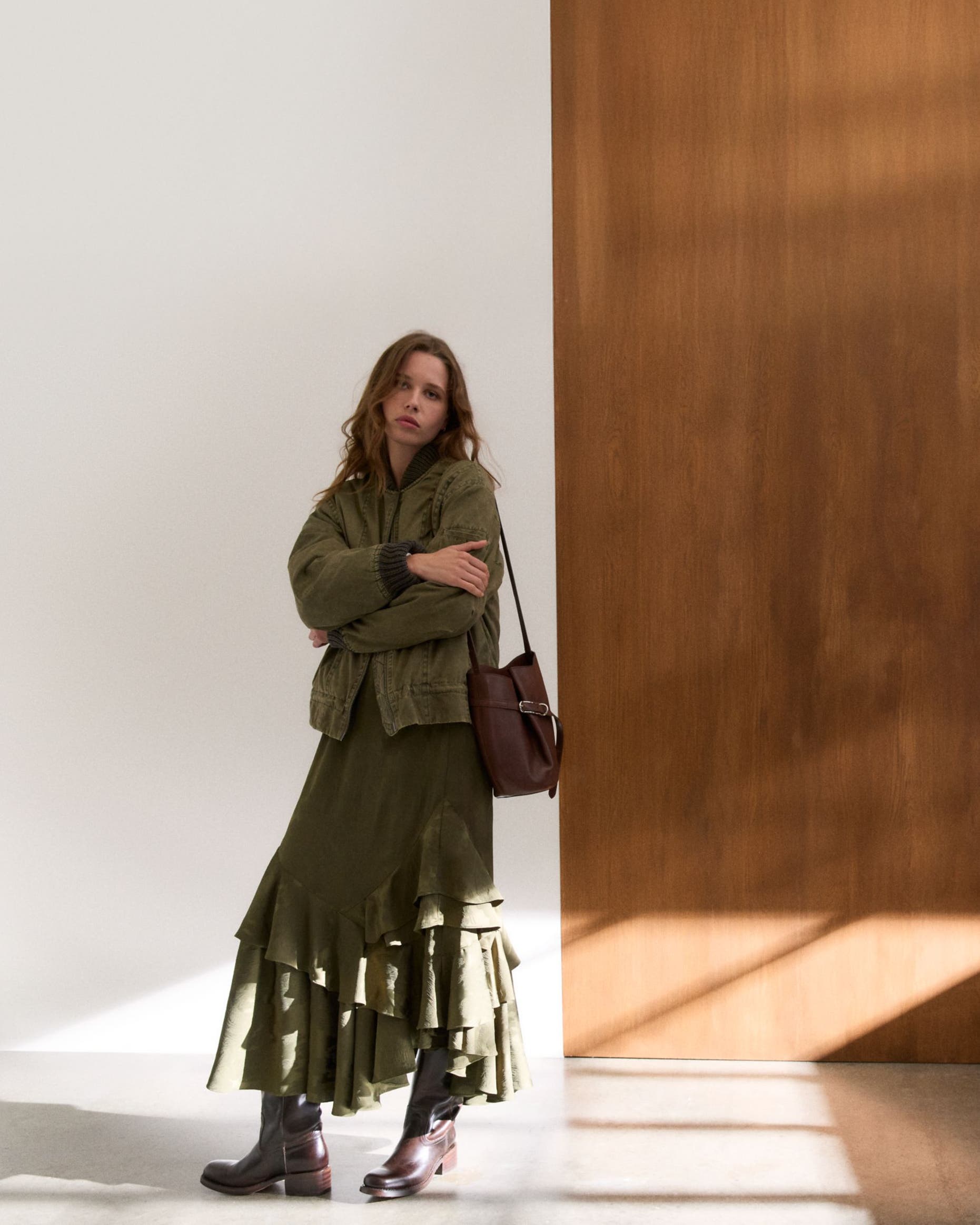 Woman wearing a bomber jacket, tiered skirt, bucket bag and boots.