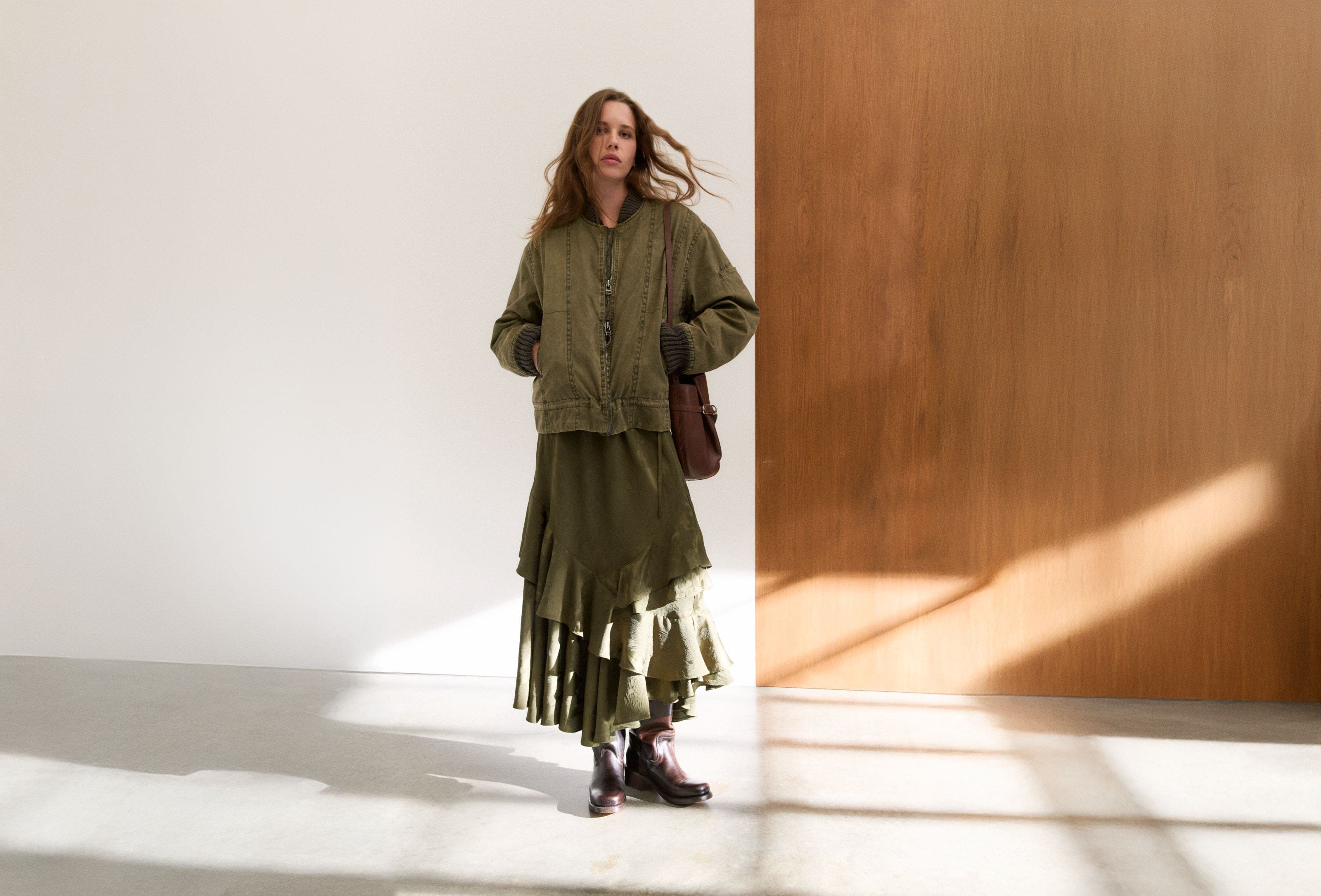 Woman wearing a bomber jacket, tiered skirt, bucket bag and boots.