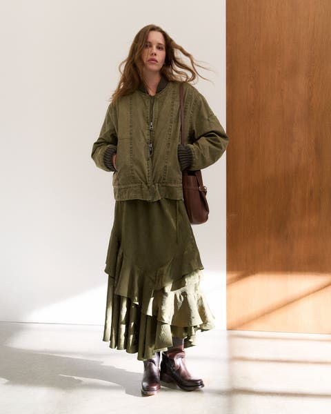 Woman wearing a bomber jacket, tiered skirt, bucket bag and boots.