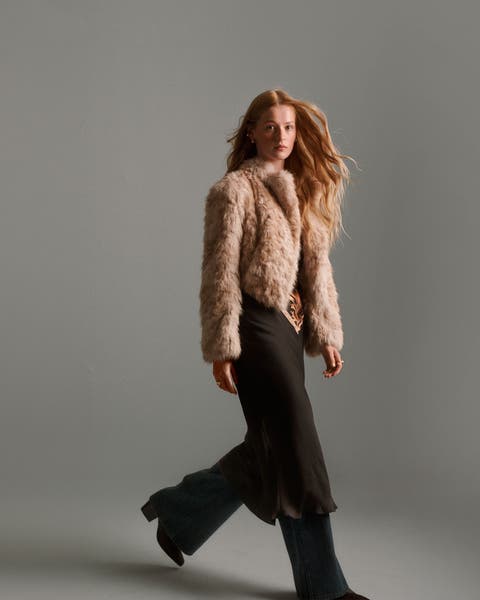 A woman wearing a fuzzy jacket over a dress with jeans.