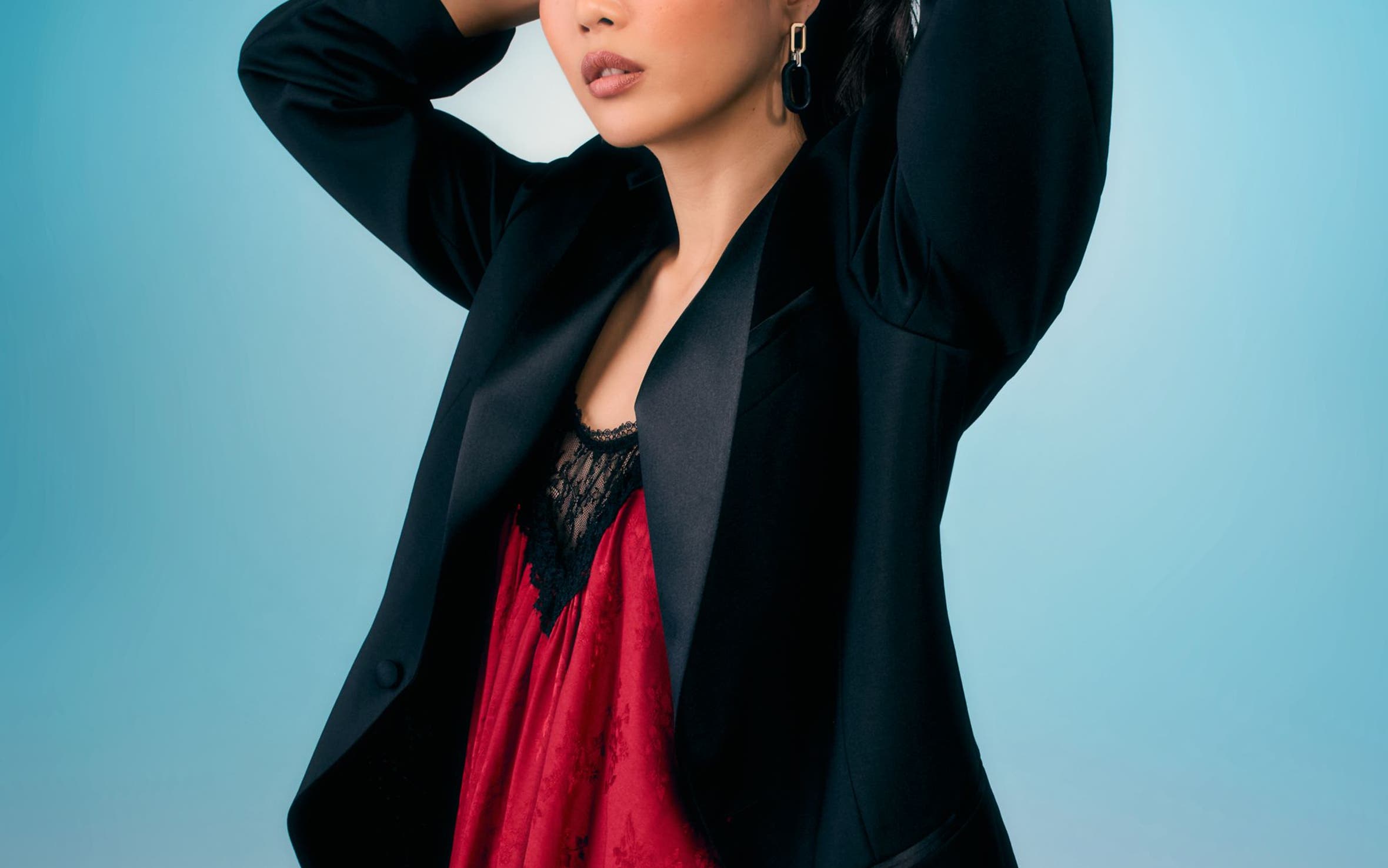 Woman wearing a black blazer over a red lace top.