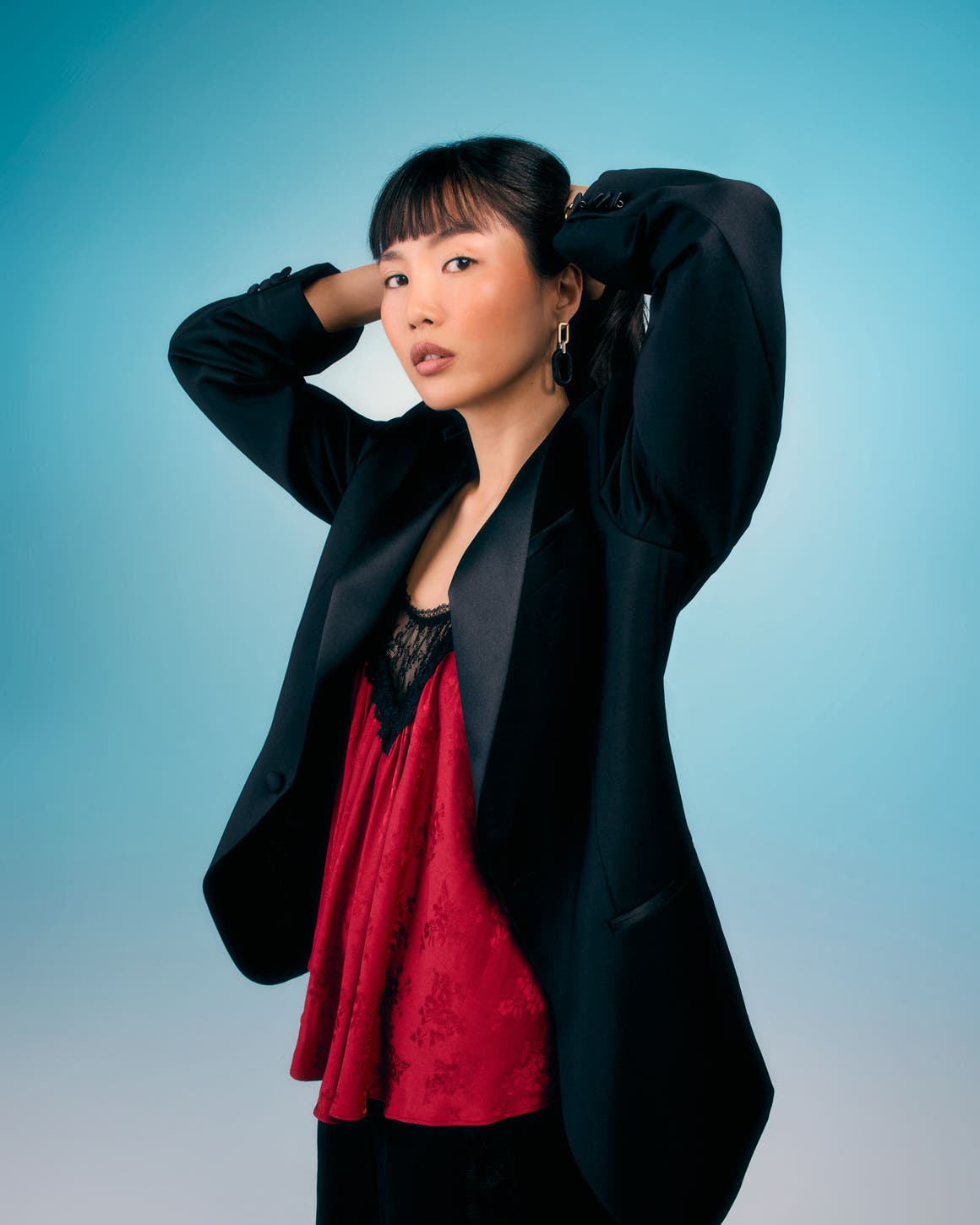 Woman wearing a black blazer over a red lace top.