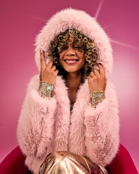 A girl with curly hair wears a fluffy pink hooded coat and metallic gold pants.