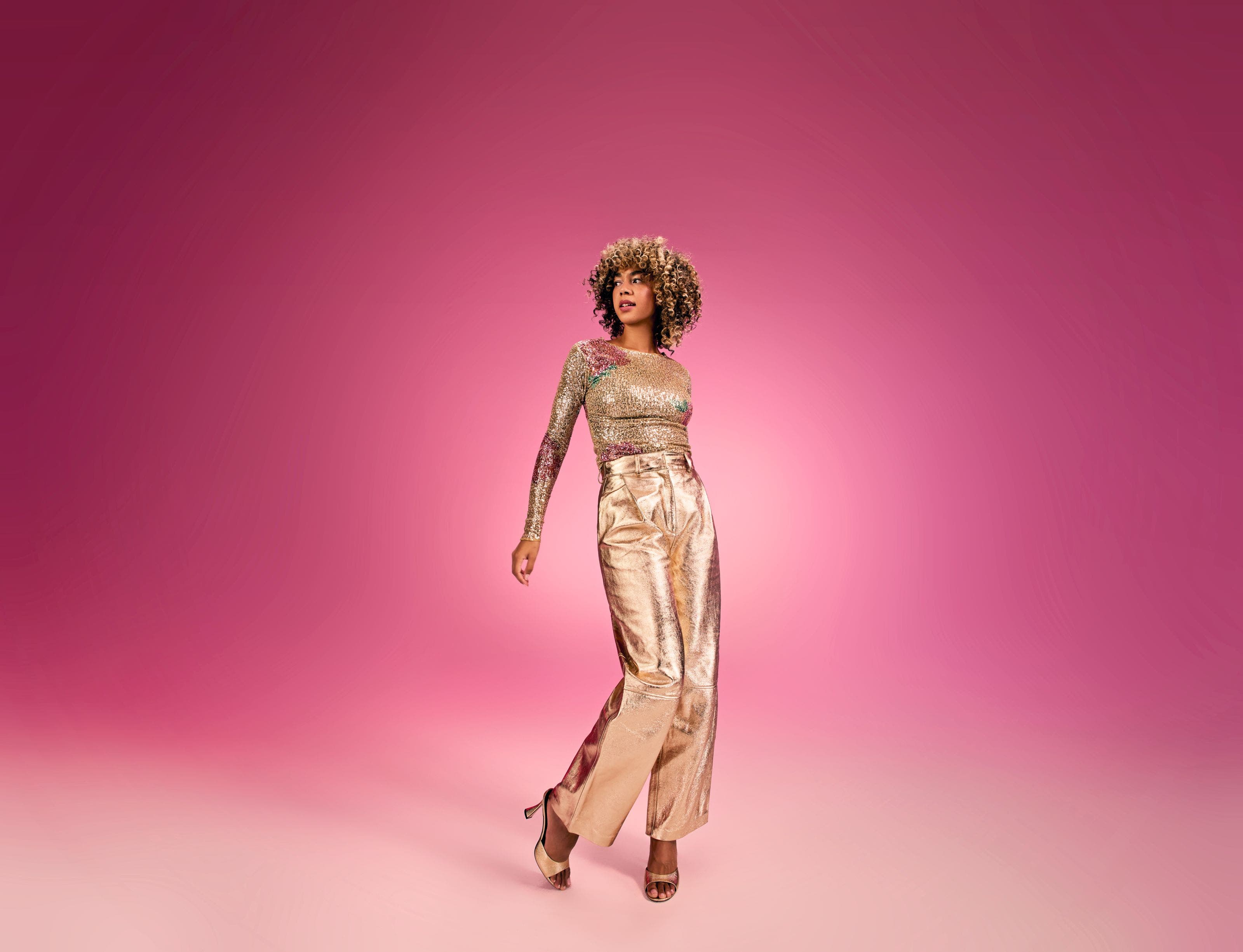 A woman wearing a gold top, gold pants and gold heels.