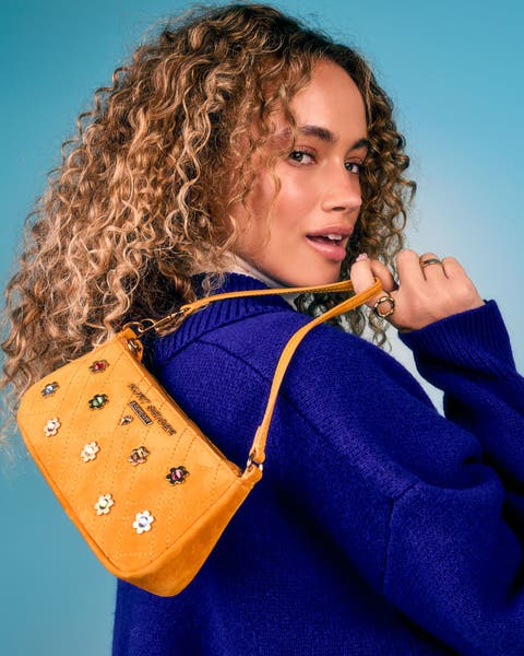Model carrying a yellow purse with floral stud embellishments and a yellow strap.
