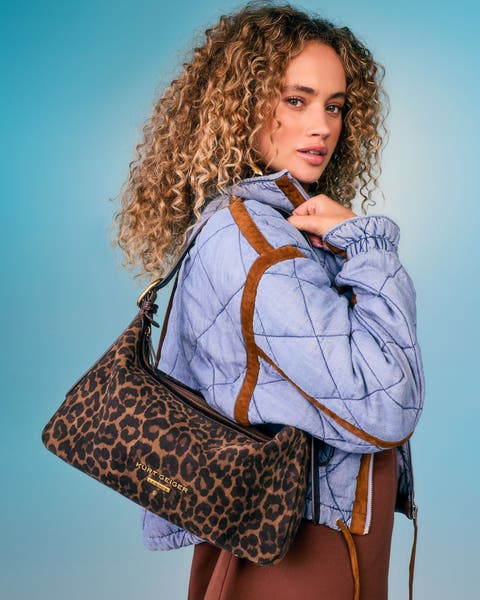 Model carrying a leopard print shoulder bag while wearing a light blue quilted jacket and brown skirt.