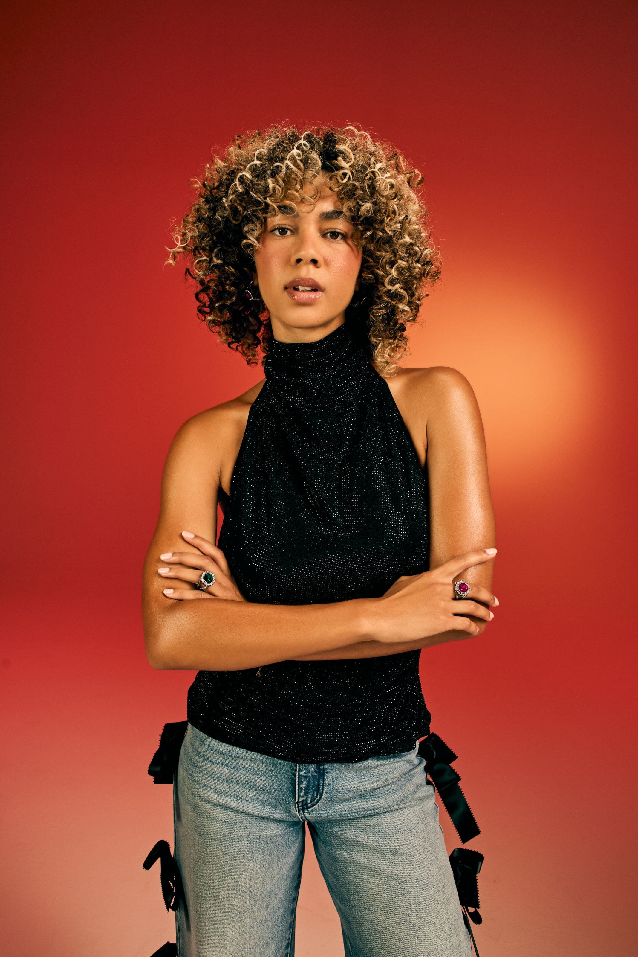 Woman in a black sparkle halter top and jeans, wearing colorful rings.