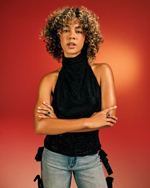 Woman in a black sparkle halter top and jeans, wearing colorful rings.