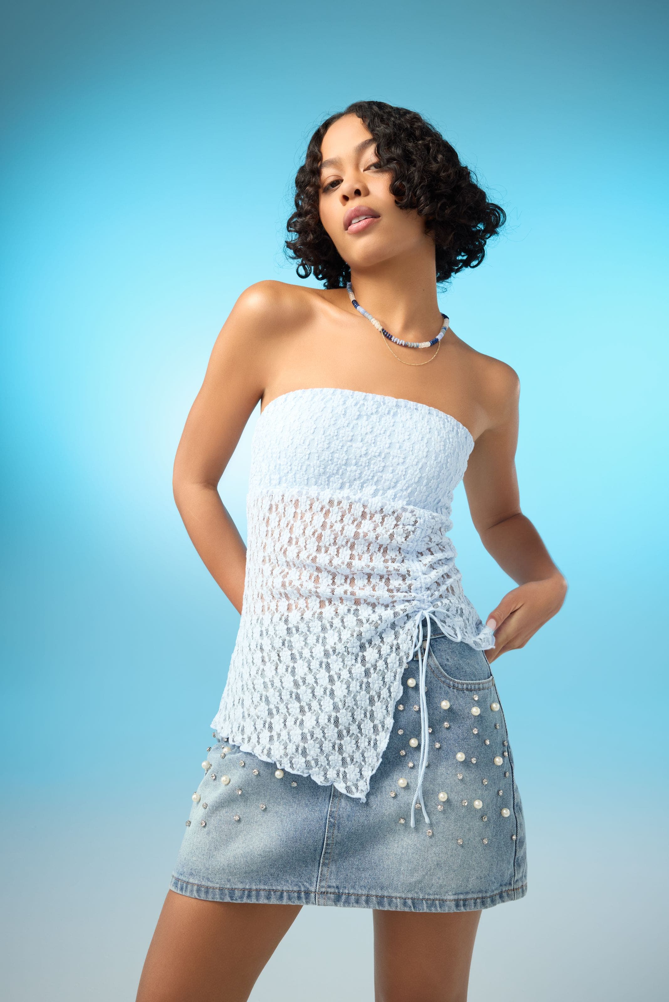 A woman wearing a strapless lace top with an embellished denim miniskirt. 