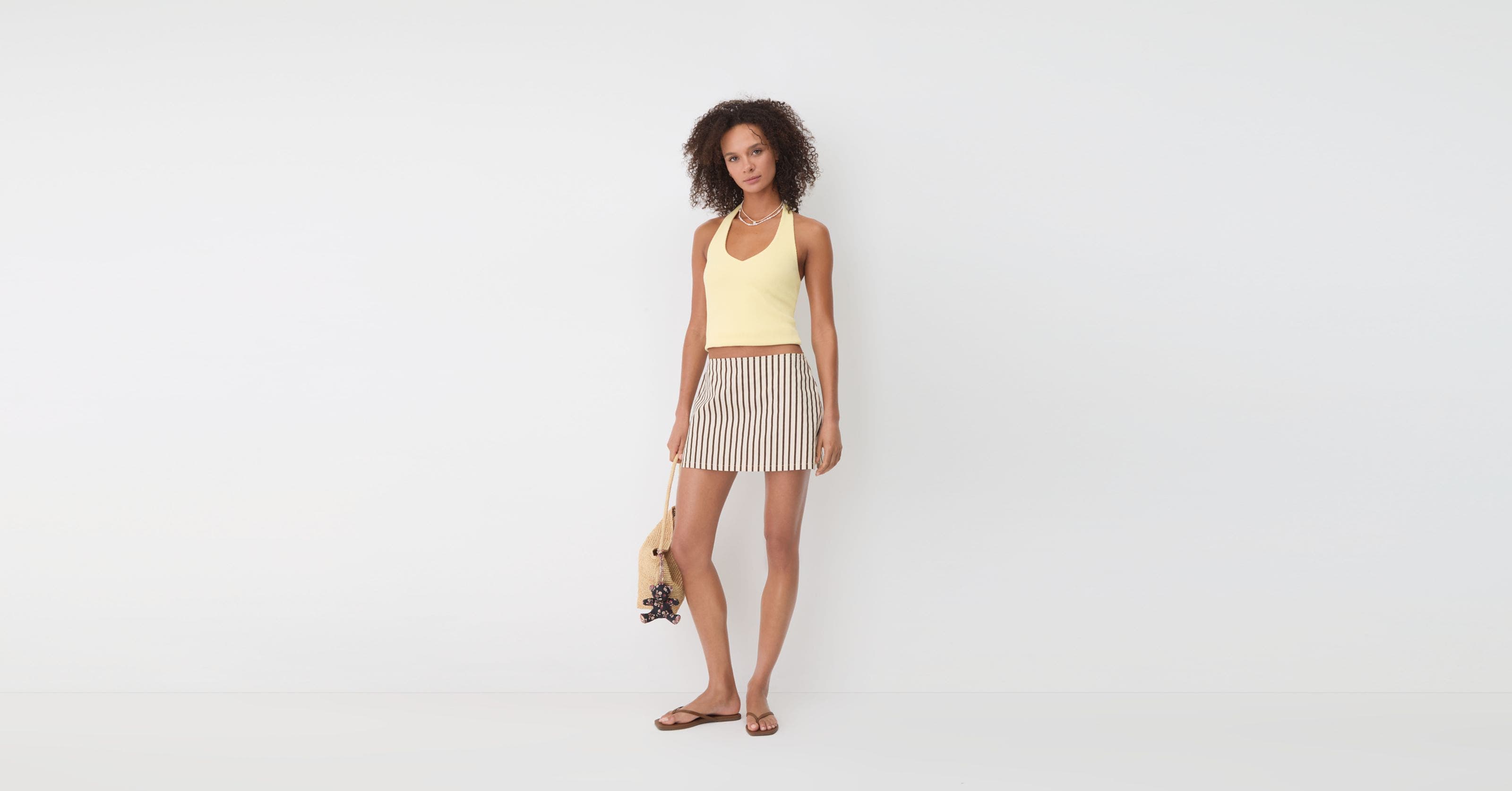Woman wearing yellow tank, mini skirt and sandals.