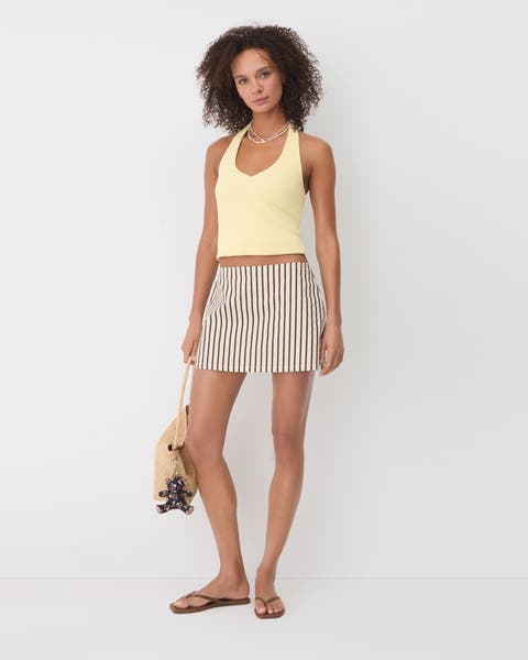 Woman wearing yellow tank, mini skirt and sandals.