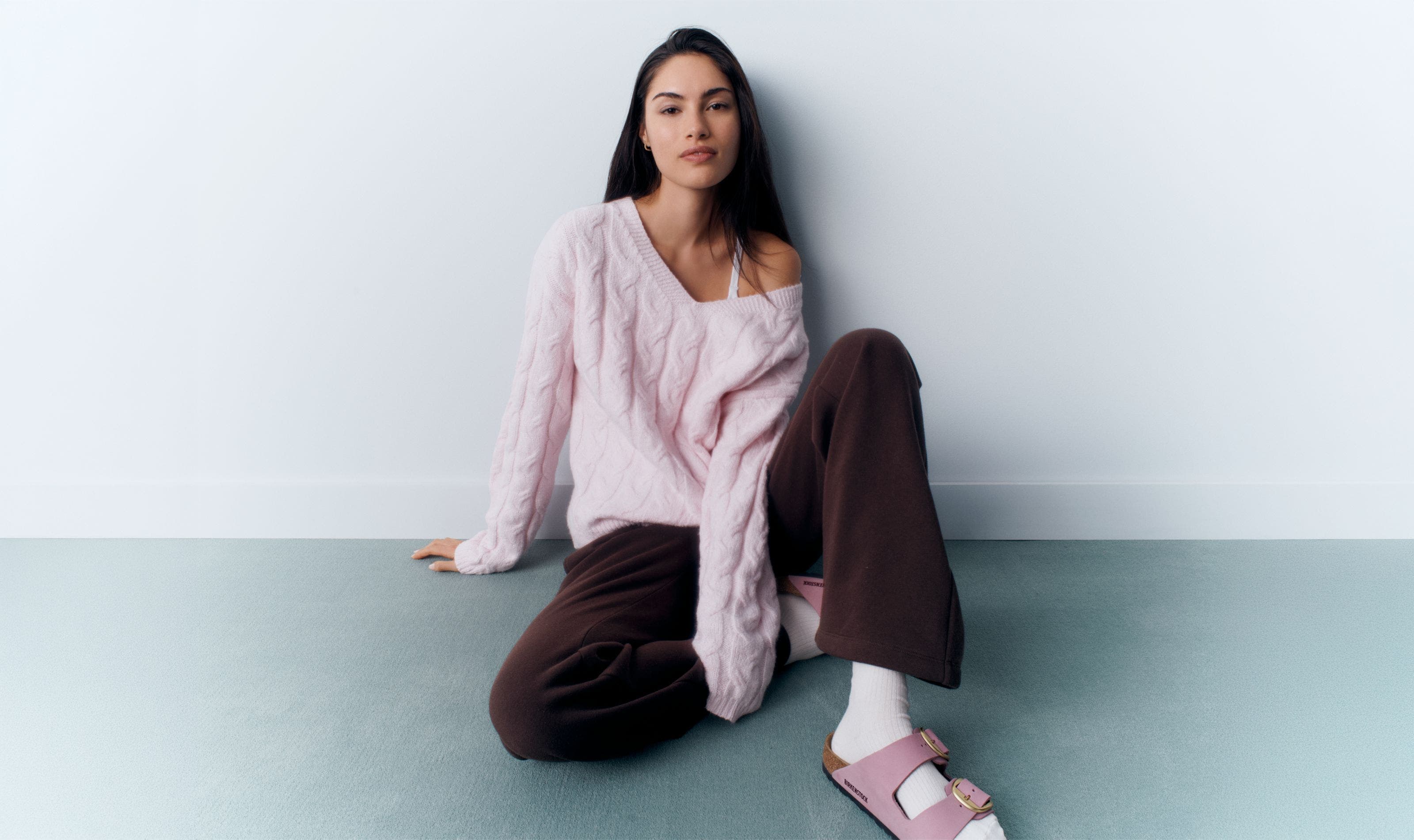 A woman wearing a pink sweater and brown pants.