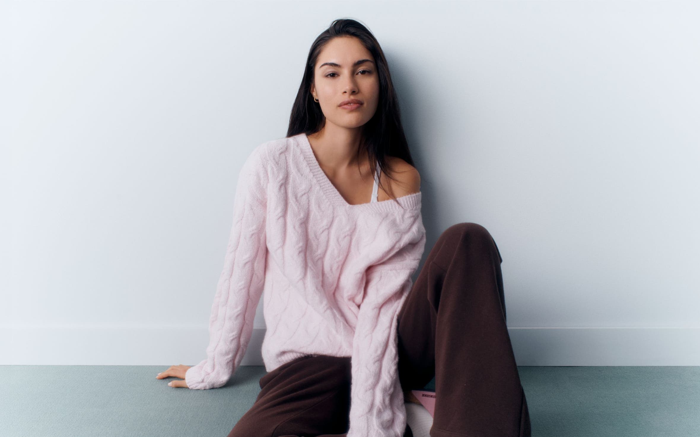 A woman wearing a pink sweater and brown pants.