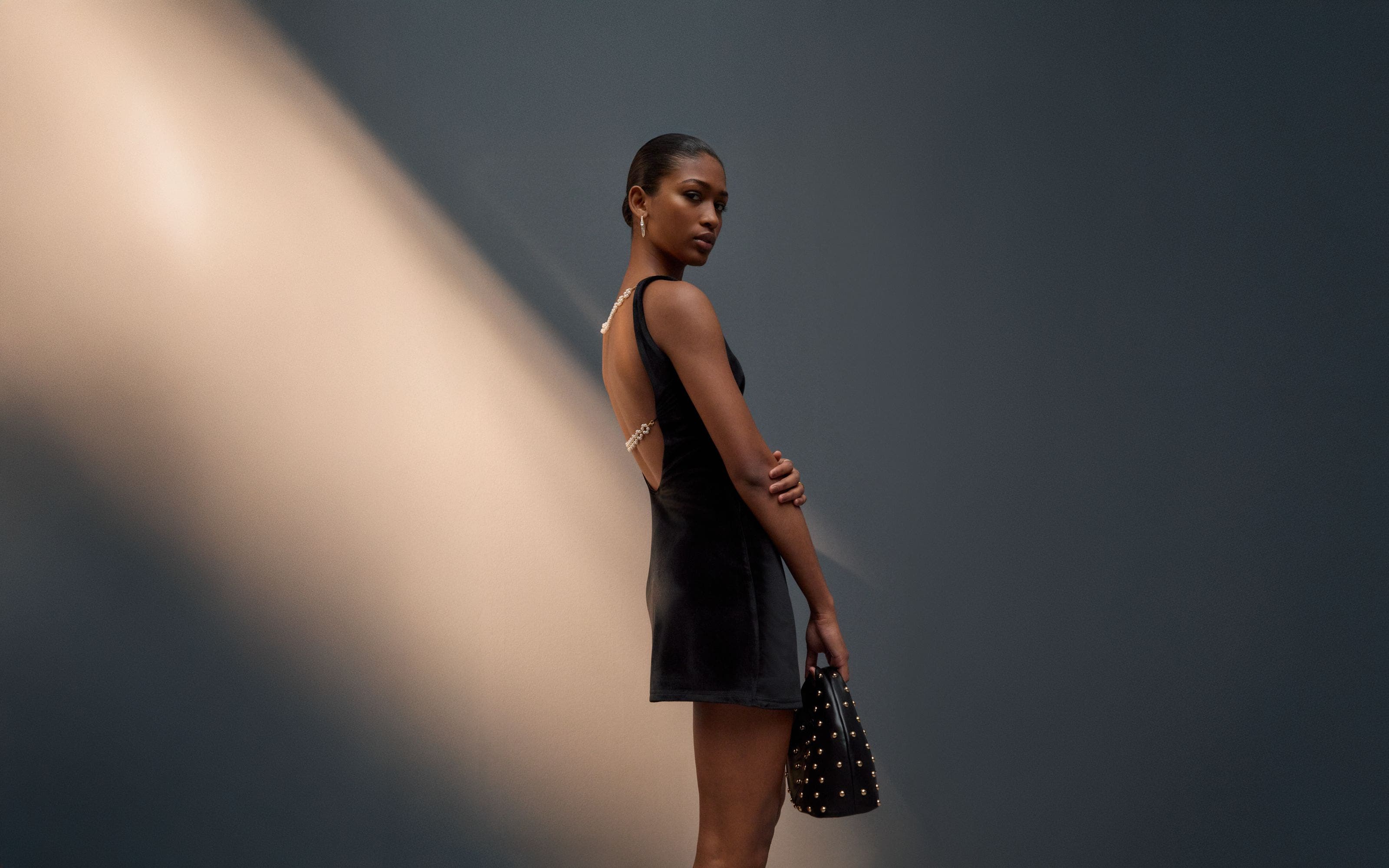 Woman wearing a little black dress and a studded handbag.