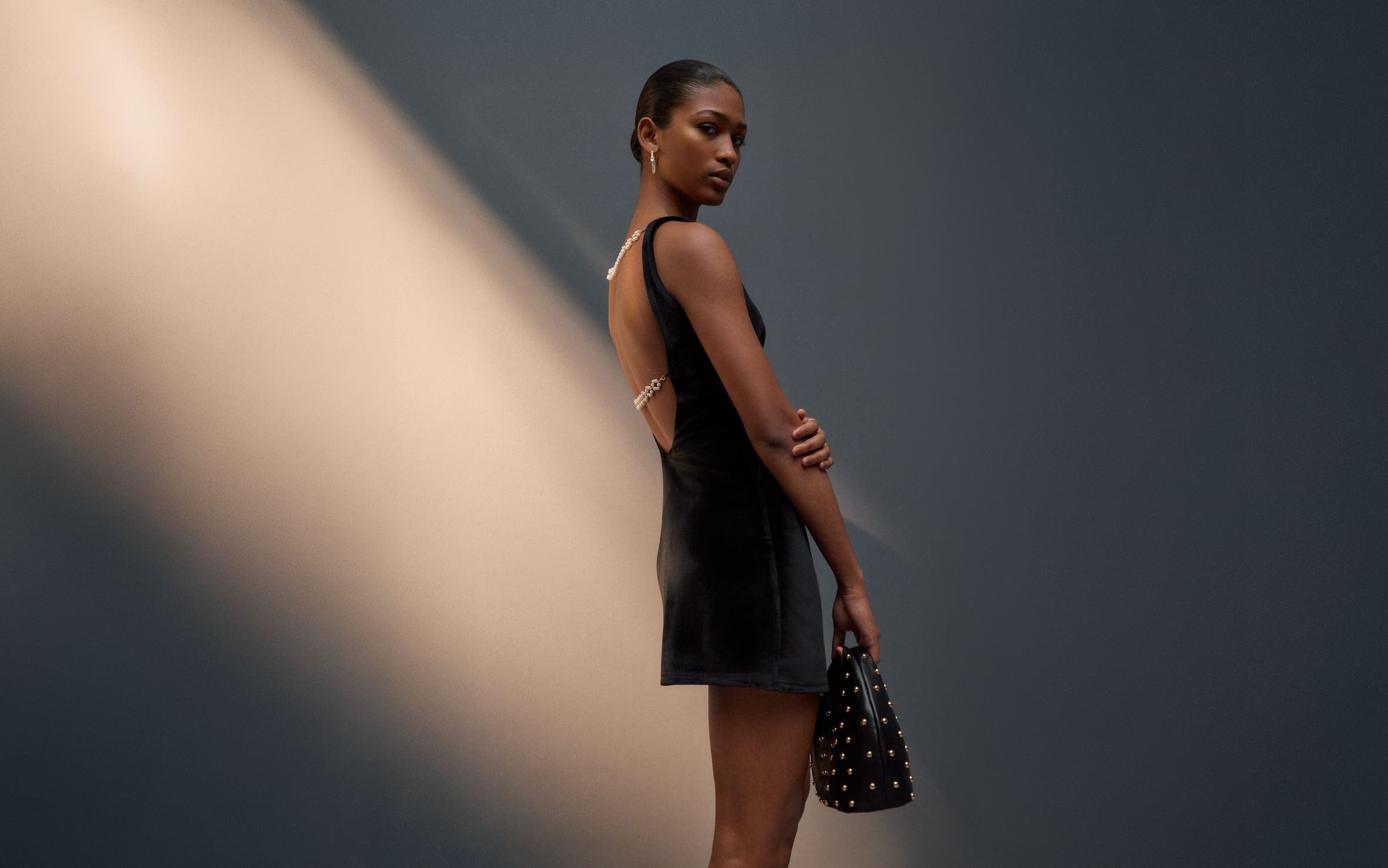 Woman wearing a little black dress and a studded handbag.
