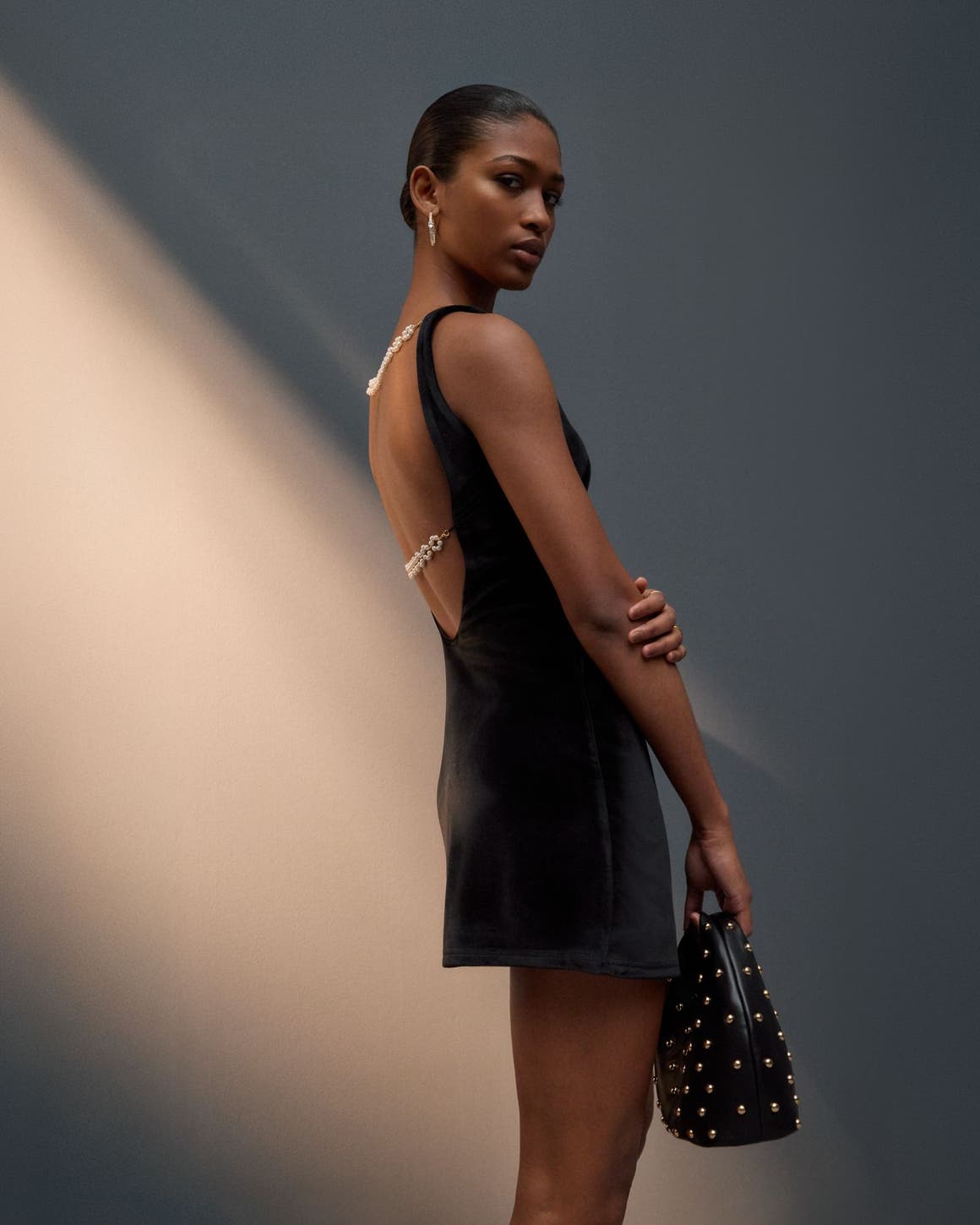 Woman wearing a little black dress and a studded handbag.