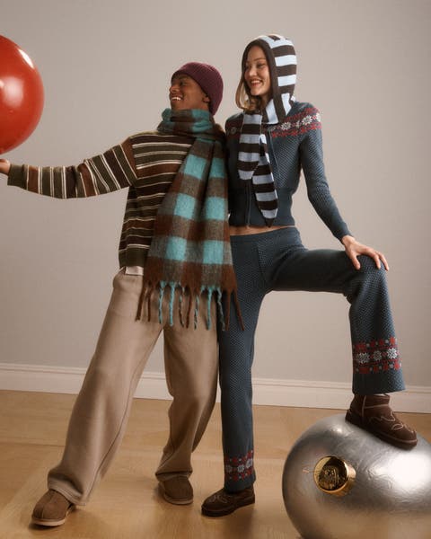 A man and woman wearing scarves, sweaters, pants and slippers.