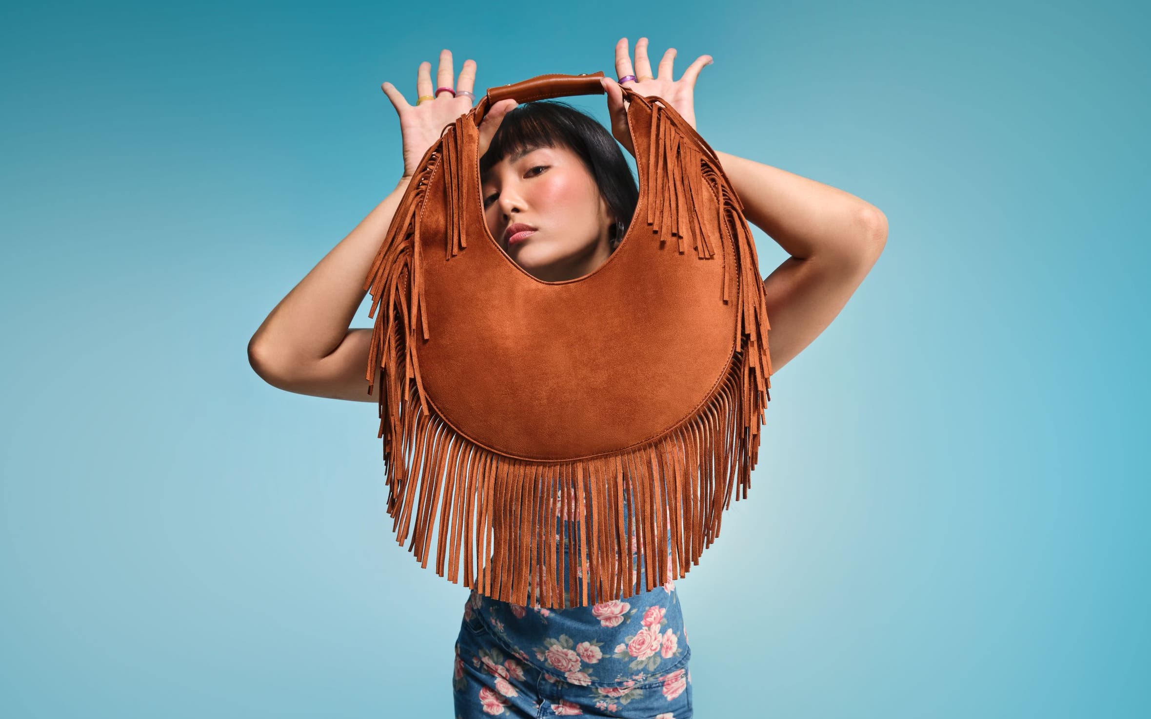 A woman holding a brown fringed handbag.
