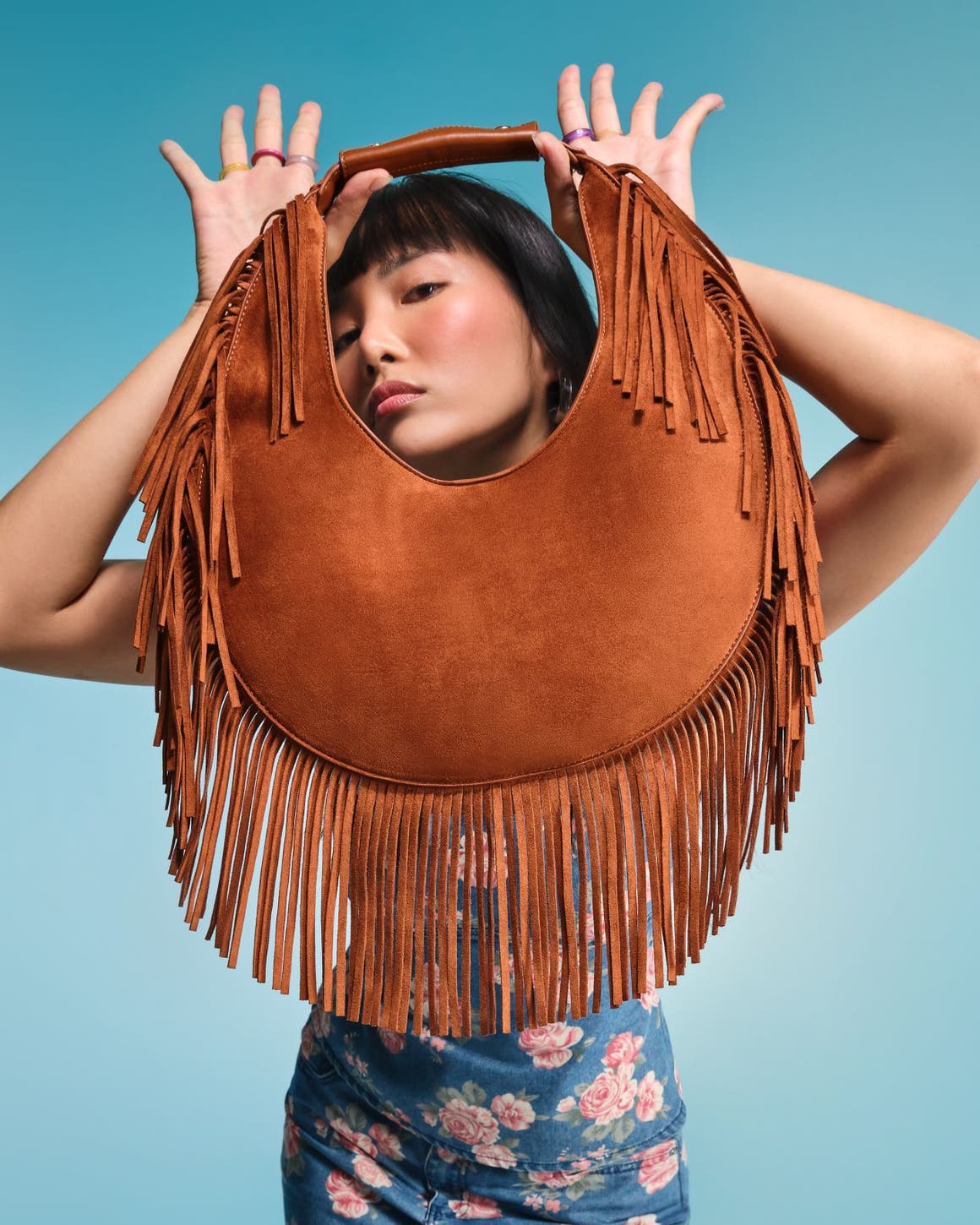 A woman holding a brown fringed handbag.