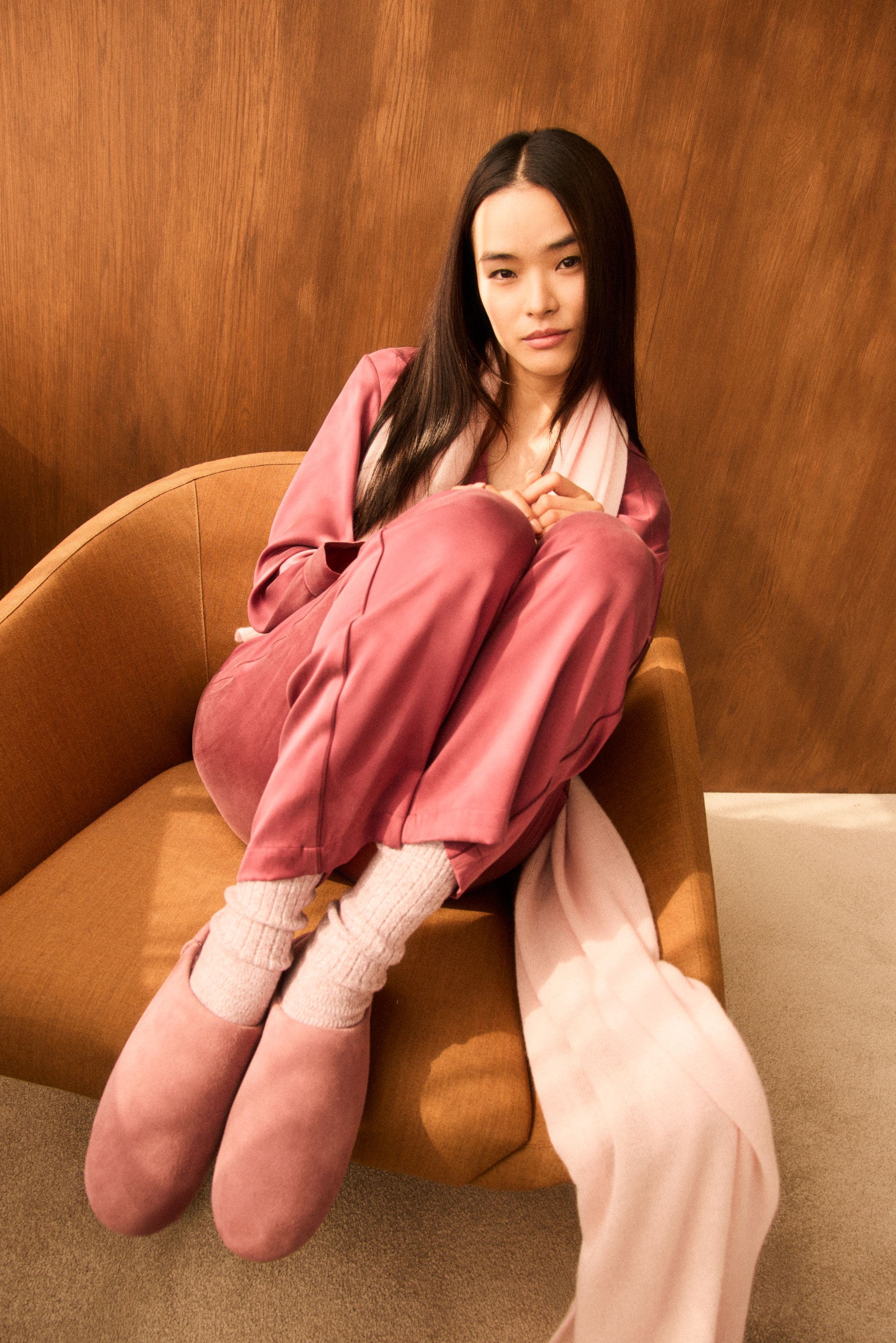 A woman wearing a pink pajama set, scarf, socks and slippers.