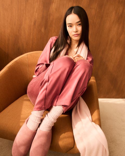 A woman wearing a pink pajama set, scarf, socks and slippers.