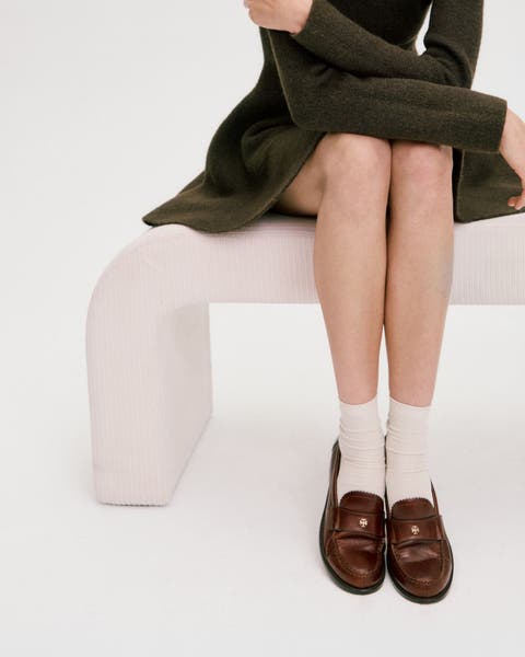 A woman wearing a dress, brown loafers and white socks.