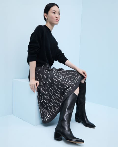 A woman wearing a sweater and skirt with knee-high boots.