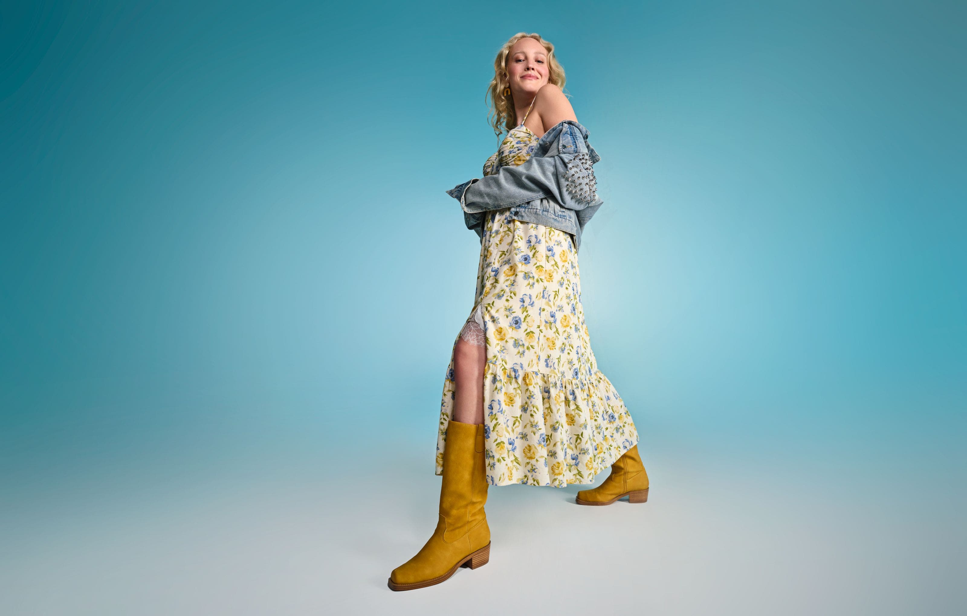 A woman wearing a floral-print maxi dress with a denim jacket and yellow boots.